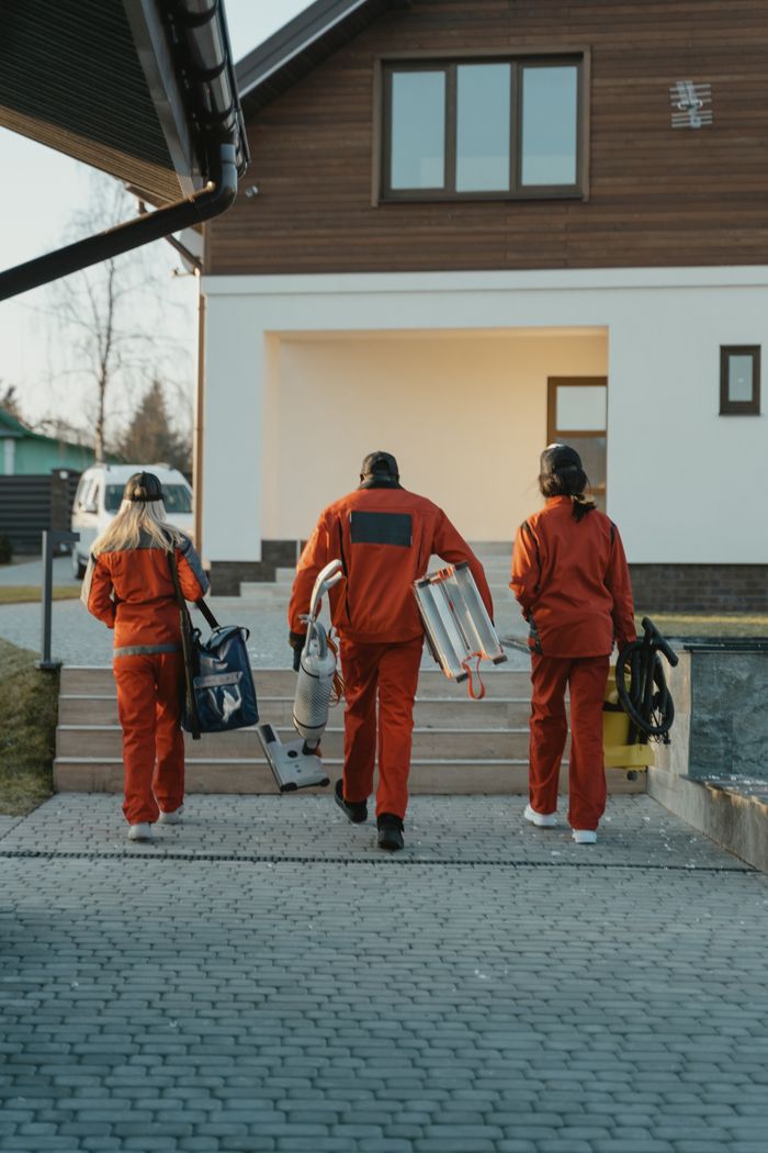 Des agents de nettoyage en uniformes rouges, munis de leur matériel, s’approchent de l’extérieur d’une maison moderne.